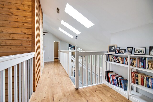 corridor with light wood finished floors, visible vents, lofted ceiling with skylight, and an upstairs landing