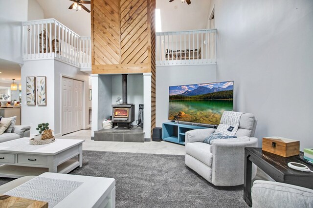 living area featuring a wood stove, carpet flooring, ceiling fan, and a towering ceiling