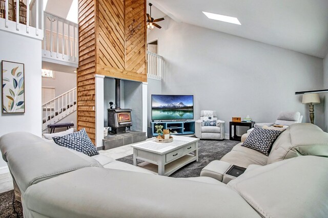 living room with high vaulted ceiling, stairway, a skylight, and a wood stove