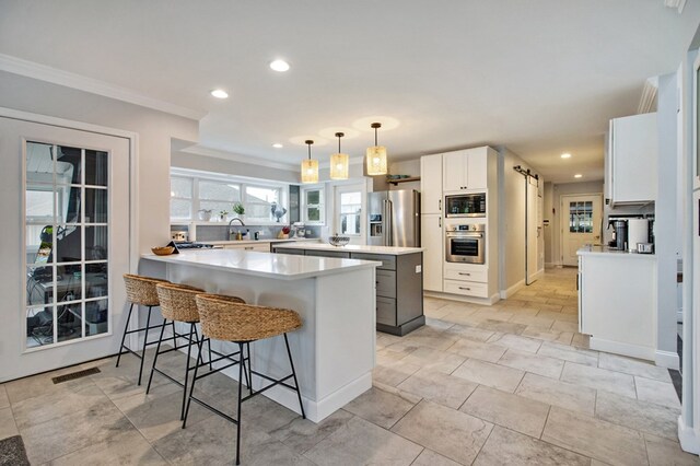 kitchen with white cabinets, appliances with stainless steel finishes, a center island, decorative light fixtures, and light countertops