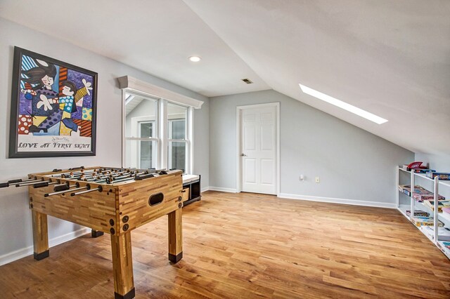 rec room with vaulted ceiling with skylight, visible vents, baseboards, and wood finished floors