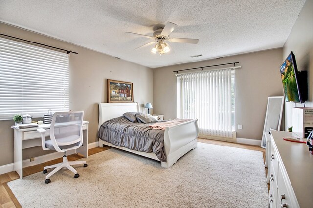 bedroom featuring light wood-style flooring, a textured ceiling, visible vents, and baseboards