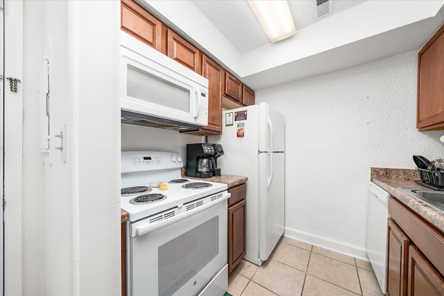 kitchen featuring white appliances, brown cabinetry, light tile patterned flooring, and baseboards