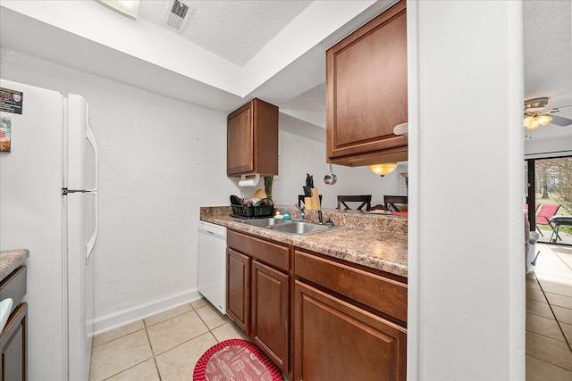 kitchen with a textured ceiling, light tile patterned flooring, white appliances, a sink, and brown cabinets