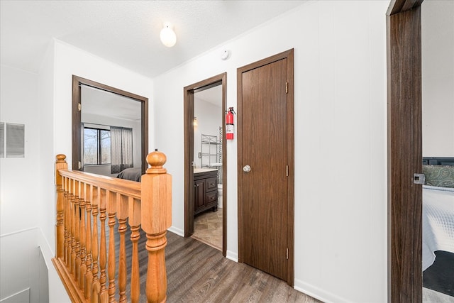 hall featuring a textured ceiling, visible vents, wood finished floors, and an upstairs landing