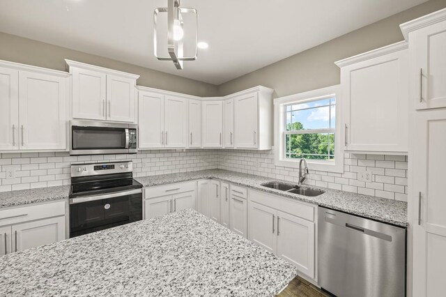 kitchen featuring stainless steel appliances, white cabinetry, a sink, and hanging light fixtures