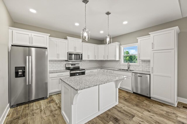 kitchen with a kitchen island, light stone counters, stainless steel appliances, white cabinetry, and a sink