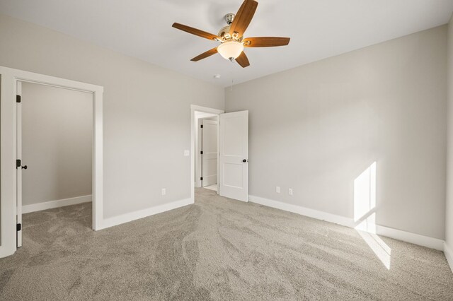 unfurnished bedroom featuring light carpet, ceiling fan, a spacious closet, and baseboards