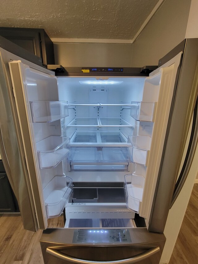 room details with refrigerator, a textured ceiling, and wood finished floors