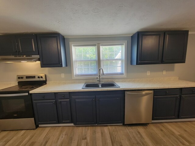 kitchen with stainless steel appliances, light countertops, light wood-style flooring, a sink, and under cabinet range hood