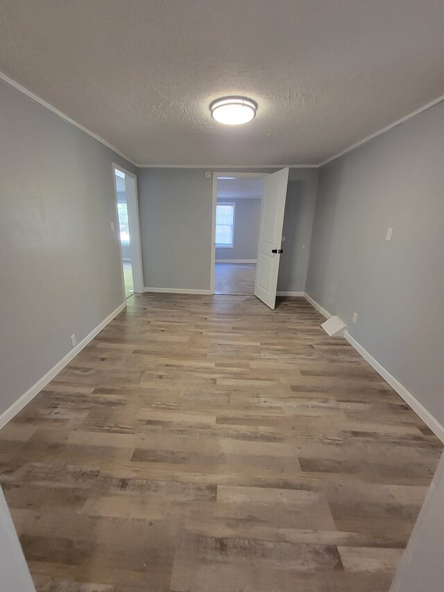 unfurnished room with light wood-style floors, a textured ceiling, baseboards, and crown molding