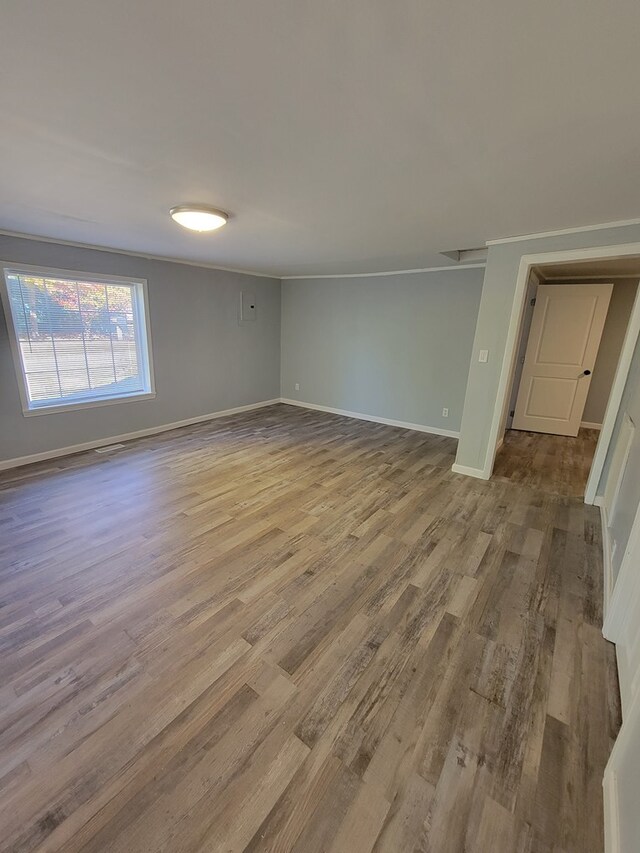 empty room with light wood finished floors, baseboards, and ornamental molding