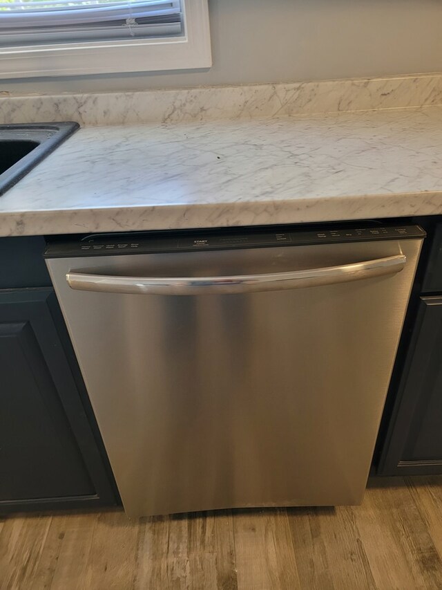 details featuring light wood-type flooring, light countertops, stainless steel dishwasher, and dark cabinetry