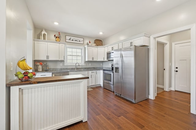 kitchen featuring appliances with stainless steel finishes, dark wood-type flooring, white cabinetry, a sink, and a peninsula