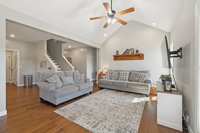 living room with dark wood-type flooring, a ceiling fan, vaulted ceiling, baseboards, and stairs