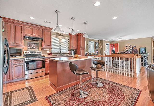 kitchen featuring light countertops, light wood-style floors, under cabinet range hood, appliances with stainless steel finishes, and decorative light fixtures