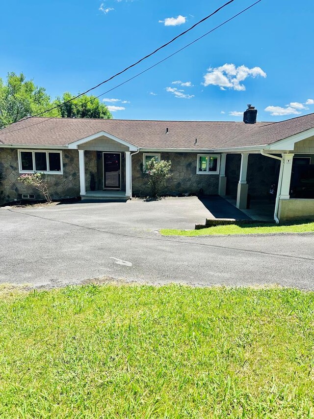 view of front facade featuring stone siding, driveway, a front lawn, and roof with shingles