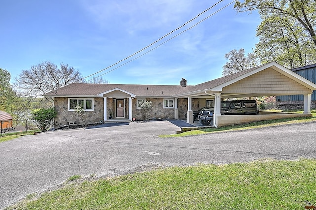 view of front of home featuring a carport, stone siding, driveway, and a chimney