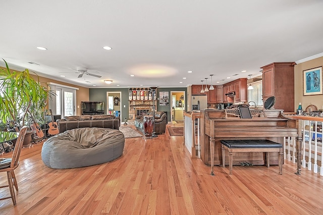 living room featuring a ceiling fan, light wood finished floors, recessed lighting, ornamental molding, and a large fireplace