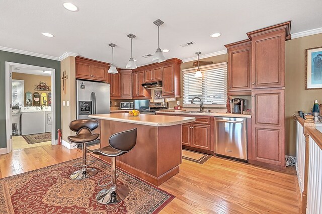 kitchen with a breakfast bar area, washing machine and clothes dryer, a sink, light countertops, and appliances with stainless steel finishes