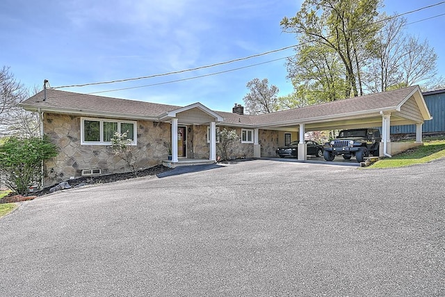 ranch-style home featuring an attached carport, a chimney, stone siding, and aphalt driveway