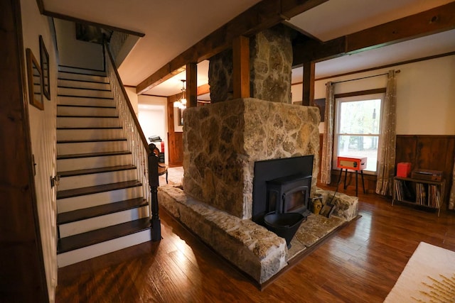 living room featuring a wood stove, stairs, dark wood-style flooring, and wainscoting