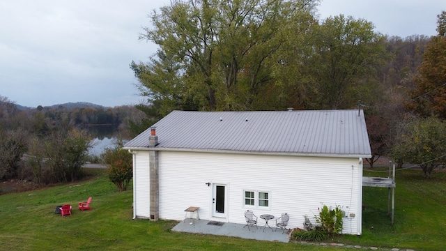 back of property featuring metal roof, a patio, a yard, and a view of trees