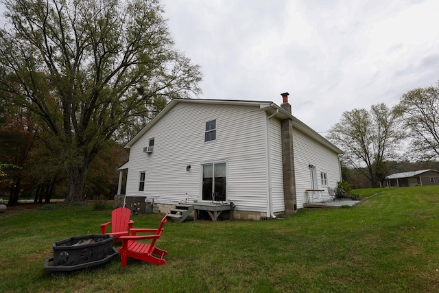 back of house featuring a fire pit, a lawn, and a chimney