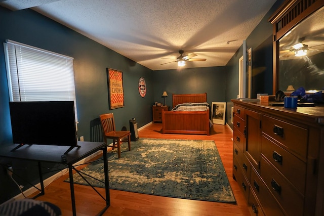 bedroom with a textured ceiling, ceiling fan, wood finished floors, and baseboards