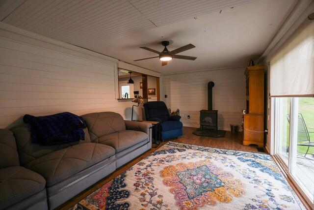 living area with ceiling fan, wood walls, wood finished floors, and a wood stove