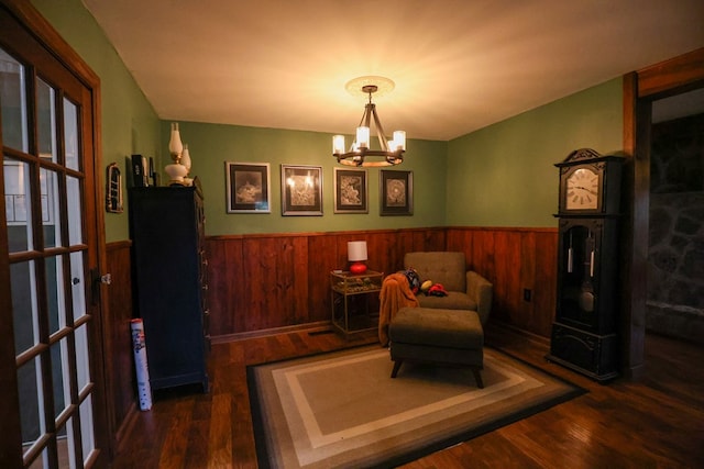 sitting room with dark wood-type flooring, wood walls, wainscoting, and an inviting chandelier