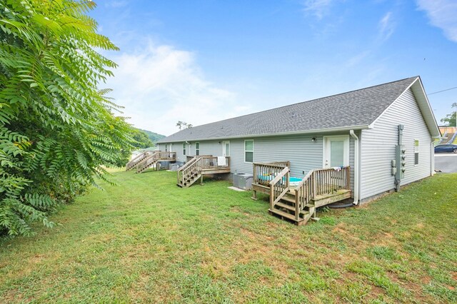 back of house with a shingled roof, stairway, a deck, and a lawn