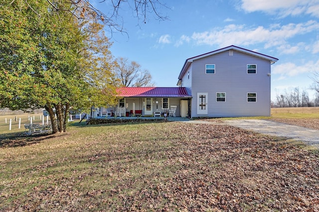 rear view of property featuring driveway, metal roof, a porch, and a yard