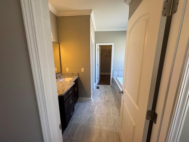 bathroom with vanity, baseboards, ornamental molding, a walk in closet, and a bathtub