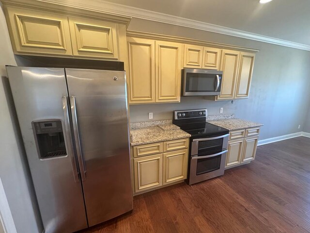 kitchen with light stone countertops, dark wood-style flooring, ornamental molding, cream cabinetry, and appliances with stainless steel finishes