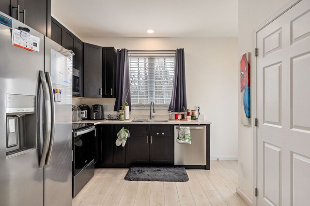 kitchen featuring appliances with stainless steel finishes, dark cabinets, light countertops, light wood-type flooring, and a sink