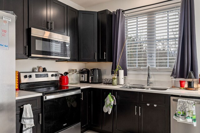 kitchen with dark cabinetry, appliances with stainless steel finishes, light countertops, and a sink