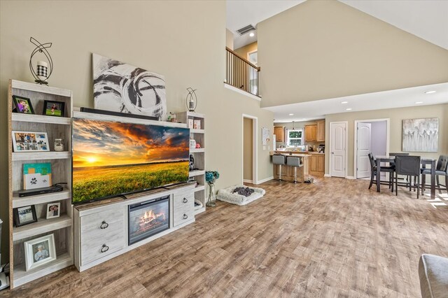 living room with light wood-style floors, a high ceiling, visible vents, and a tile fireplace