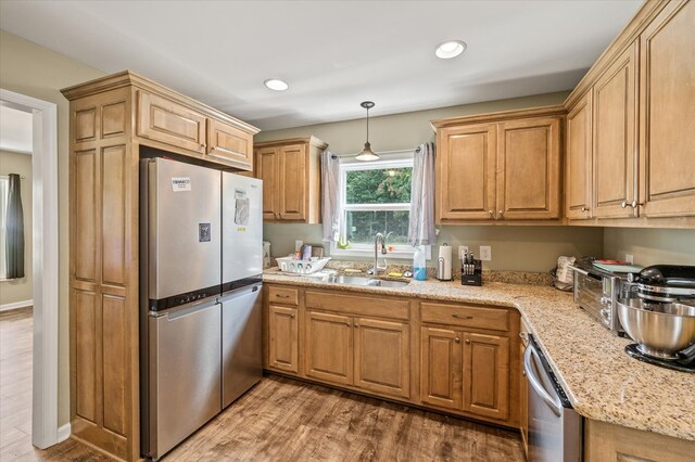 kitchen featuring wood finished floors, light stone countertops, stainless steel appliances, pendant lighting, and a sink