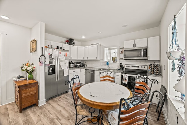 kitchen featuring light stone countertops, light wood-style flooring, appliances with stainless steel finishes, and white cabinets