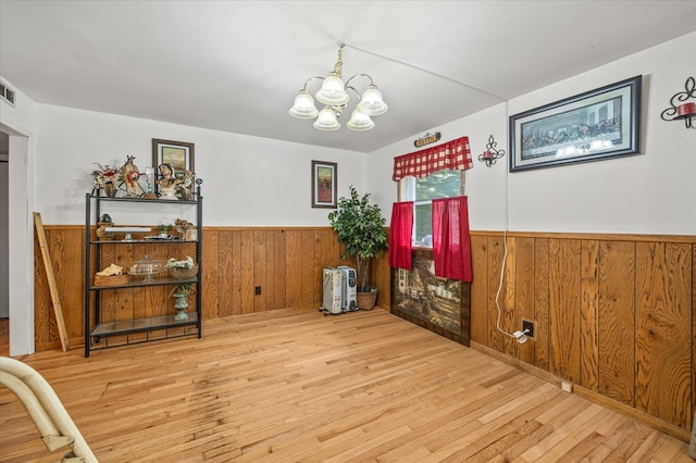 dining area featuring light wood finished floors, visible vents, a wainscoted wall, wood walls, and a notable chandelier