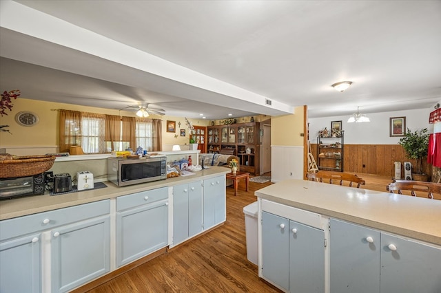 kitchen featuring a wainscoted wall, stainless steel microwave, open floor plan, and light countertops