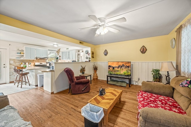 living room with wainscoting, ceiling fan, and light wood finished floors