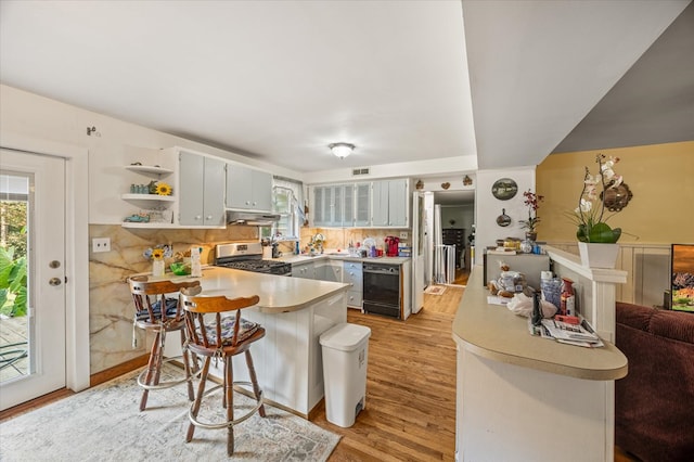 kitchen featuring a breakfast bar, light wood finished floors, light countertops, stainless steel gas stove, and a peninsula