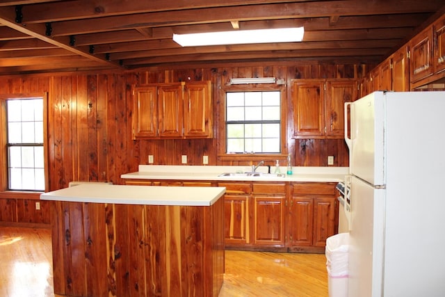 kitchen featuring light wood-style flooring, wooden walls, a sink, light countertops, and freestanding refrigerator