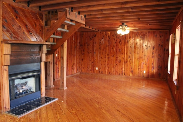 unfurnished living room featuring ceiling fan, wooden walls, a fireplace, wood finished floors, and stairway