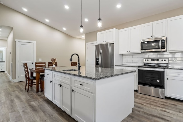 kitchen with wood finished floors, an island with sink, a sink, stainless steel appliances, and backsplash