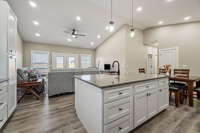 kitchen with a sink, dark wood-style floors, white cabinetry, stone counters, and hanging light fixtures