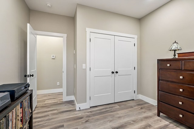 bedroom with light wood-type flooring, baseboards, and a closet