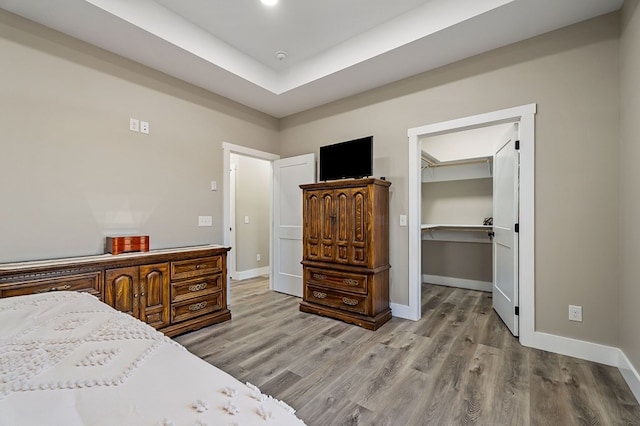 bedroom with a spacious closet, baseboards, a tray ceiling, wood finished floors, and a closet